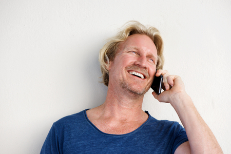 Close up portrait of smiling man by white wall and making phone callの写真素材