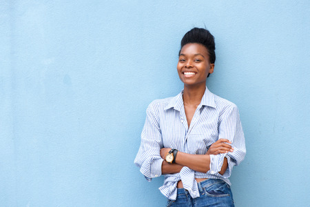 Portrait of african american woman smiling with arms crossed on blue backgroundの写真素材