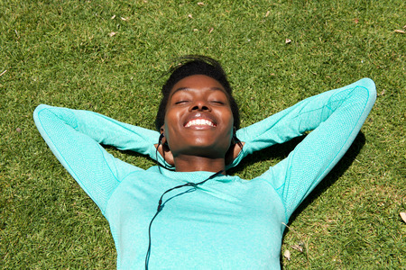 Portrait of young black woman lying down on grass listening to music with earphonesの写真素材