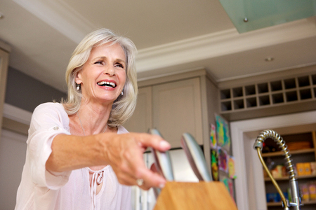 Close up portrait of smiling older woman in kitchen with knife blockの写真素材