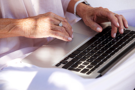 Close up portrait of older woman hands typing on laptop computerの写真素材