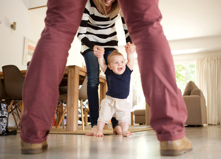 Portrait of cute baby boy learning to walk with mother and father at homeの写真素材