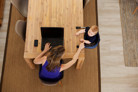 Top view portrait of mother working on laptop with baby sitting by tableの写真素材