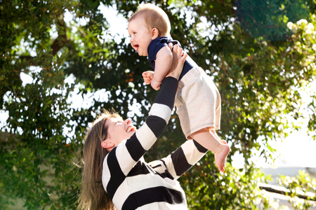 Portrait of happy mother holding up her baby son outdoors