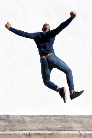 Rear view portrait of young african man jumping in air on sidewalk outdoorsの写真素材