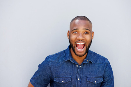Close up portrait of excited young african man laughing against gray wall