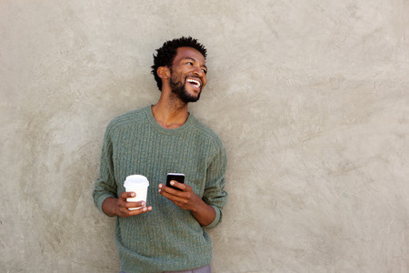 Portrait of laughing african american man with coffee and mobile phone