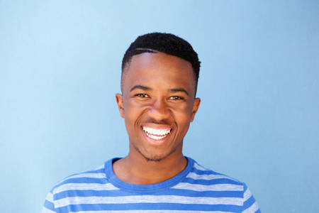 Close up portrait of african male youth smiling against blue wallの写真素材