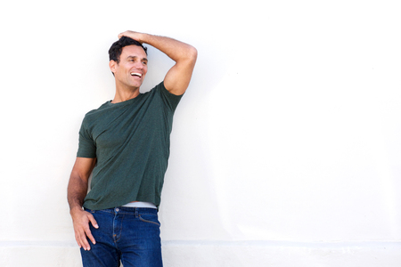 Portrait of happy middle age man leaning against white wall and laughing with hand in hairの写真素材