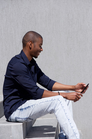 Side portrait of smiling black man sitting on steps looking at digital tabletの写真素材