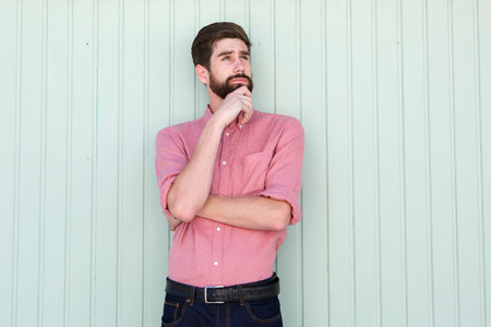 Portrait of pensive young man standing alone with hand to chinの写真素材