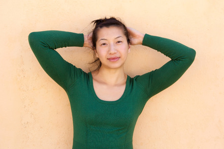 Close up portrait of relaxed asian woman standing with hands behind headの写真素材
