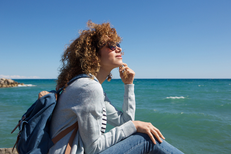 Portrait of young woman sitting by seaside thinkingの写真素材