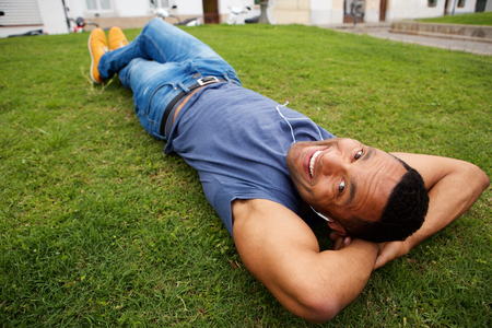 Close up portrait of happy young african man lying in grass and smilingの写真素材