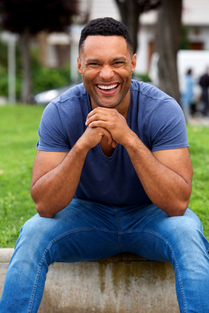 Portrait of young african man sitting outdoors and laughingの写真素材