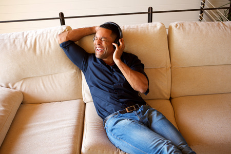 Portrait of young black man sitting in living room and enjoying listening songs on headphones