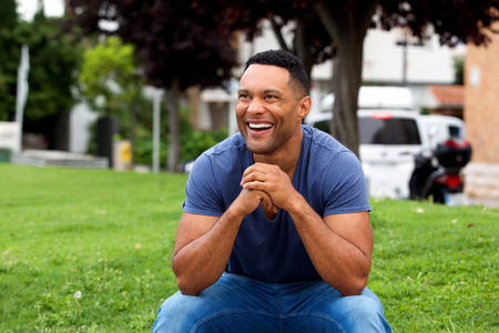 Portrait of cheerful young african guy sitting outdoors and laughingの写真素材