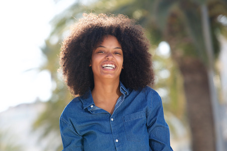 Portrait of happy young black woman outside by palm trees smiling