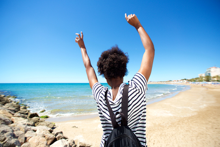 Portrait from behind of young black woman enjoying on the beach with her hands raisedの写真素材