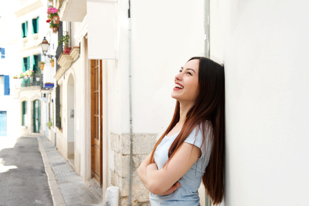 Side portrait of beautiful woman standing in street laughing with arms crossedの写真素材