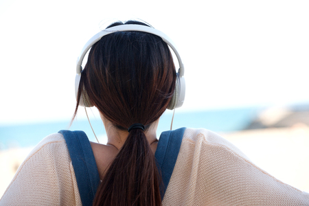 Rear portrait of woman sitting by beach with headphonesの写真素材
