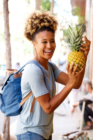 Portrait of laughing black woman standing outdoors with pineappleの写真素材
