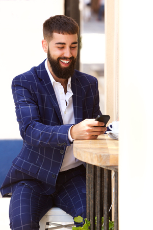 Portrait of happy man in business suit sitting with mobile phoneの写真素材