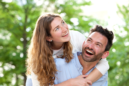 Close up portrait of laughing boyfriend carrying beautiful girlfriend outside in parkの写真素材