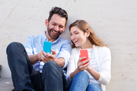Portrait of beautiful couple sitting together holding mobile phonesの写真素材