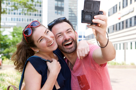Close up portrait of laughing couple taking self portrait outside with cameraの写真素材