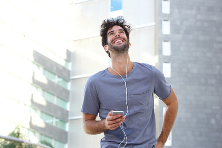 Portrait of cheerful man walking in city with headphones and mobile phoneの写真素材