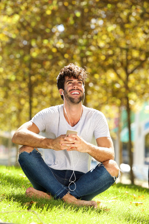 Full body portrait of happy man sitting in grass listening to musicの写真素材