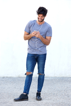 Full body portrait of cheerful man with mobile phone listening to musicの写真素材