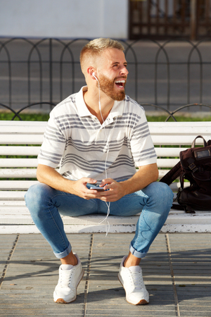Portrait of young man laughing with mobile phone and earphonesの写真素材