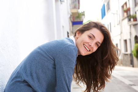 Portrait of smiling woman leaning against wall by streetの写真素材