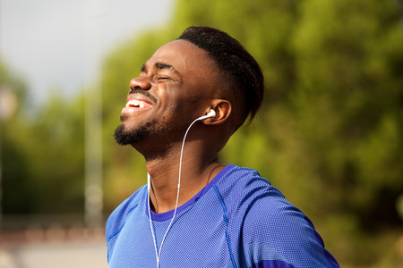 Portrait of happy young black man laughing with earphones in parkの写真素材