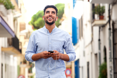 Portrait of happy young arabic man laughing with mobile phone and earphones in the cityの写真素材