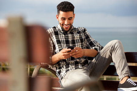 Portrait of happy young arabic man sending text message on mobile phone の写真素材