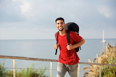 Portrait of happy young man walking with backpack by the seaの写真素材
