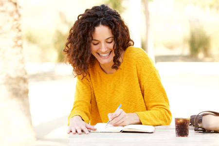 Portrait of young woman sitting at table writing in diaryの写真素材