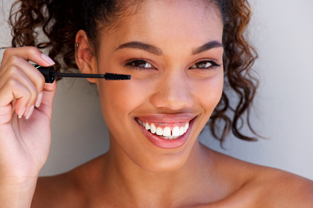 Close up portrait of beautiful young black woman putting on mascara の写真素材