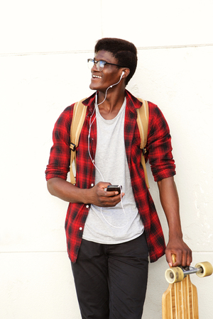 Portrait of happy young black man standing with mobile phone and skateboardの写真素材