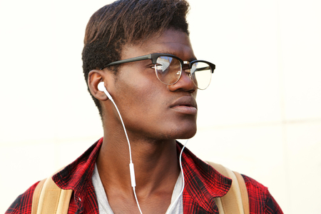 Close up young black guy with eyeglasses and earphones looking awayの写真素材
