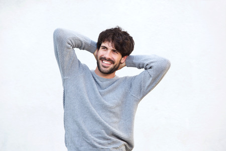 Portrait of handsome young man smiling with hands behind head against white background