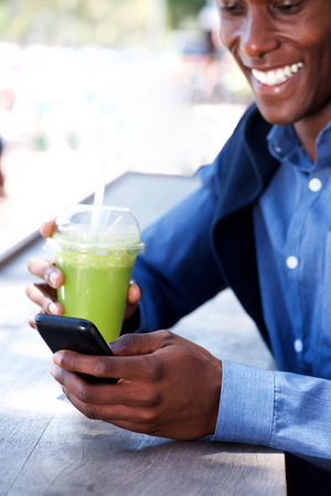 Portrait of young black man smiling with juice drink and cellphoneの写真素材