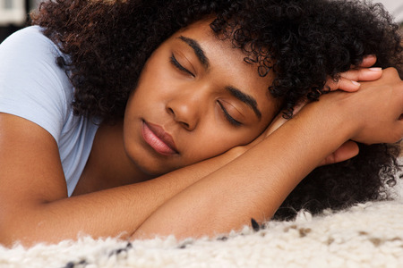 Close up portrait of young african american girl lying on floor with eyes closed, taking a nap.の写真素材