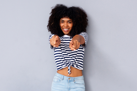 Portrait of smiling young black woman pointing fingers against gray backgroundの写真素材
