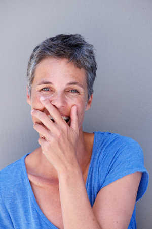 Close up portrait of happy older woman laughing with hand covering mouthの写真素材