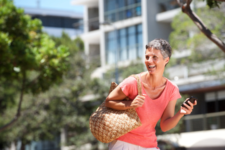 Portrait of happy woman walking outside with cellphoneの写真素材