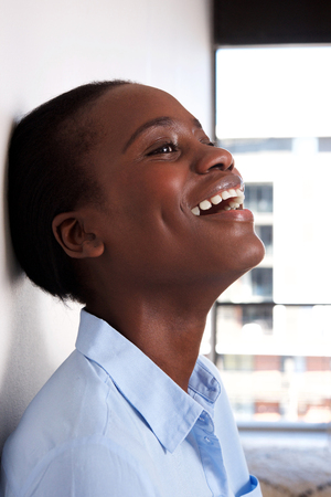 Close up portrait of happy black woman leaning against wall and smiling の写真素材